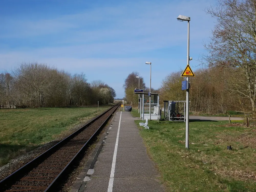 Haltepunkt Tating: schmaler Bahnsteig mit Laterne und kleinem Wartehäuschen neben dem Gleis, gesäumt von Bäumen