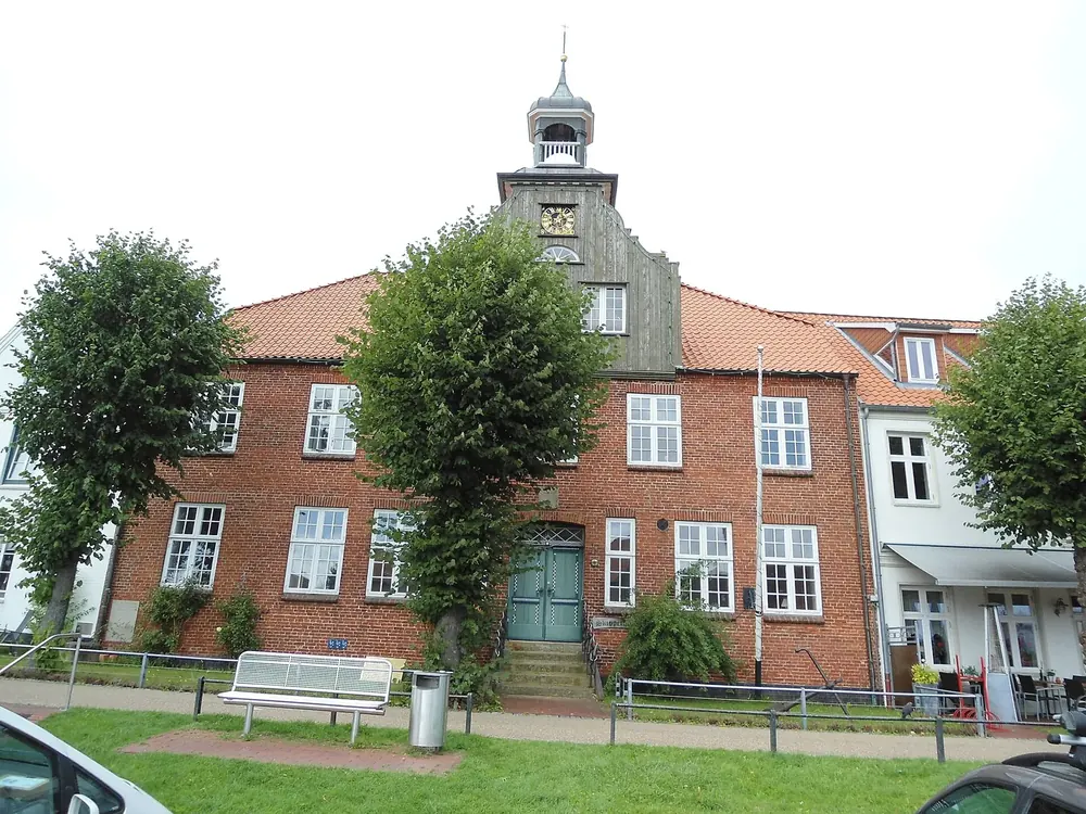 Schifferhaus am historischen Hafen von Tönning: Backsteinbau mit Uhrturm, davor Rasen und Bäume