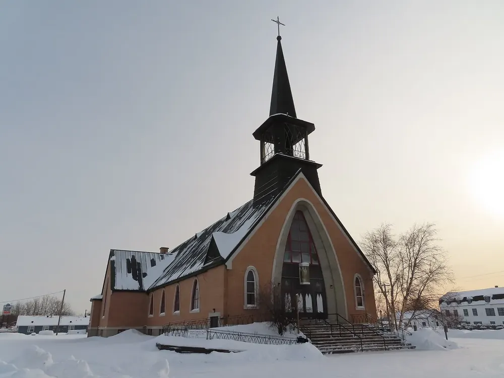 St.-Joseph-Kathedrale in Fort Smith im Winter: Backsteinkirche mit spitzem Turm hinter verschneitem Vorplatz