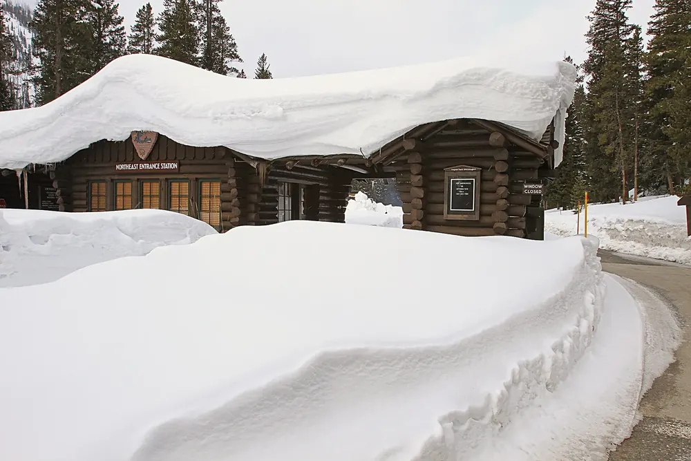 Nordosteingang des Yellowstone im April: Blockhaus-Eingangsstation mit meterhohem Schnee auf Dach und Straßenrand