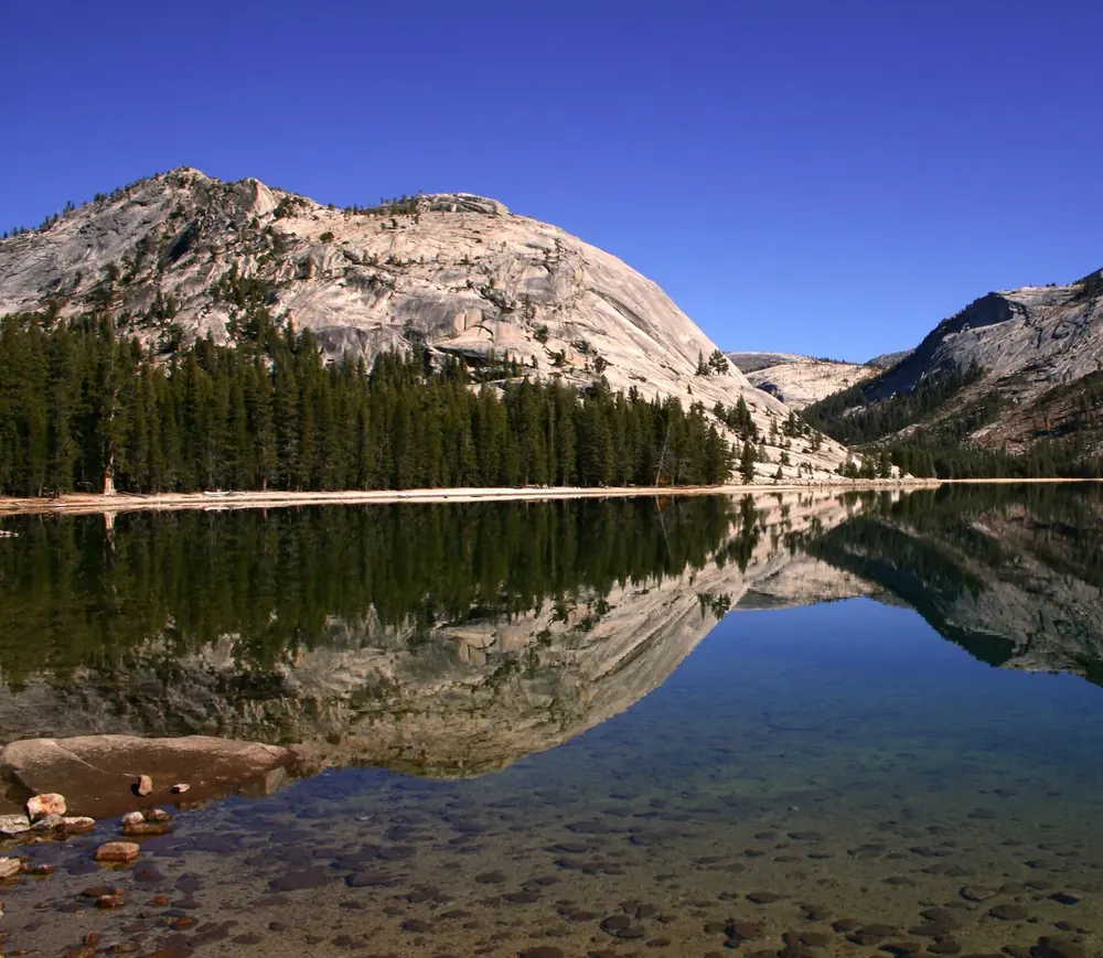 Tenaya Lake: glasklarer Bergsee, in dem sich eine Granitkuppe und dunkler Nadelwald spiegeln