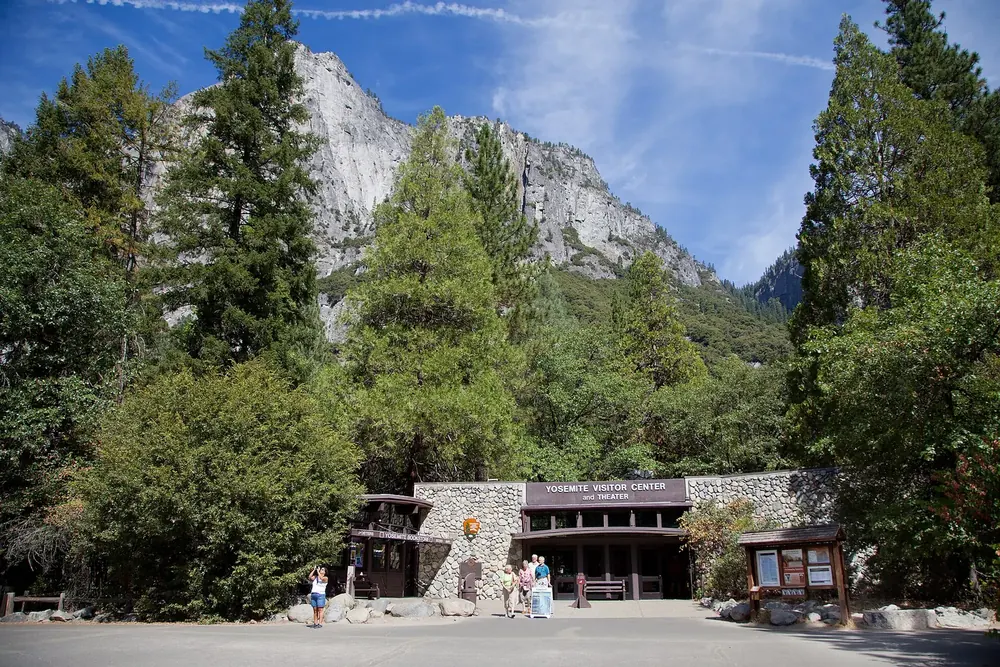 Besucherzentrum im Yosemite Village: flacher Bau mit Holzvordach zwischen hohen Nadelbäumen und Granitwänden