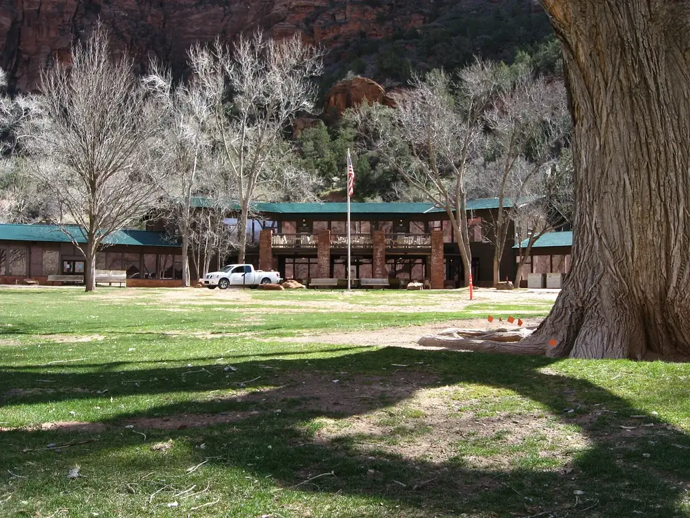 Zion Lodge: lang gestrecktes Hauptgebäude hinter einer Rasenfläche mit großen Pappeln unter roten Felswänden