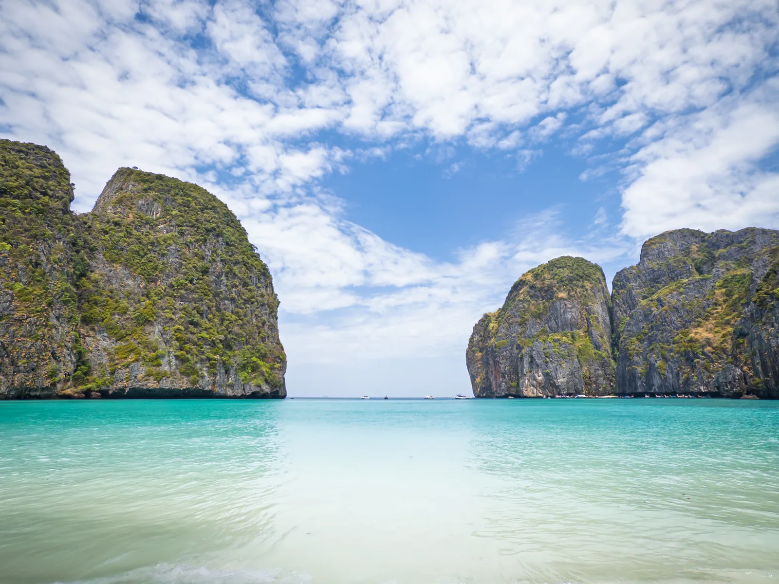 Der leere Sandstrand der Maya Bay auf Ko Phi Phi Le, flaches türkisfarbenes Wasser und links und rechts die Kalkfelsen am Eingang der Bucht