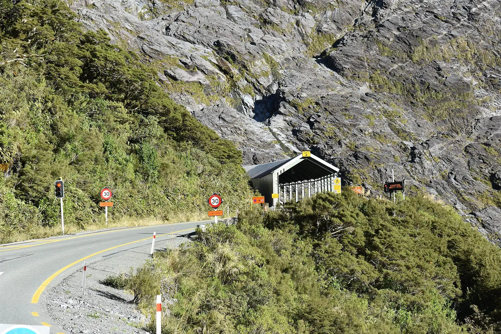 Das Westportal des Homer Tunnels an der Straße zum Milford Sound, mit Ampel und Schutzdach vor einer steilen Granitwand