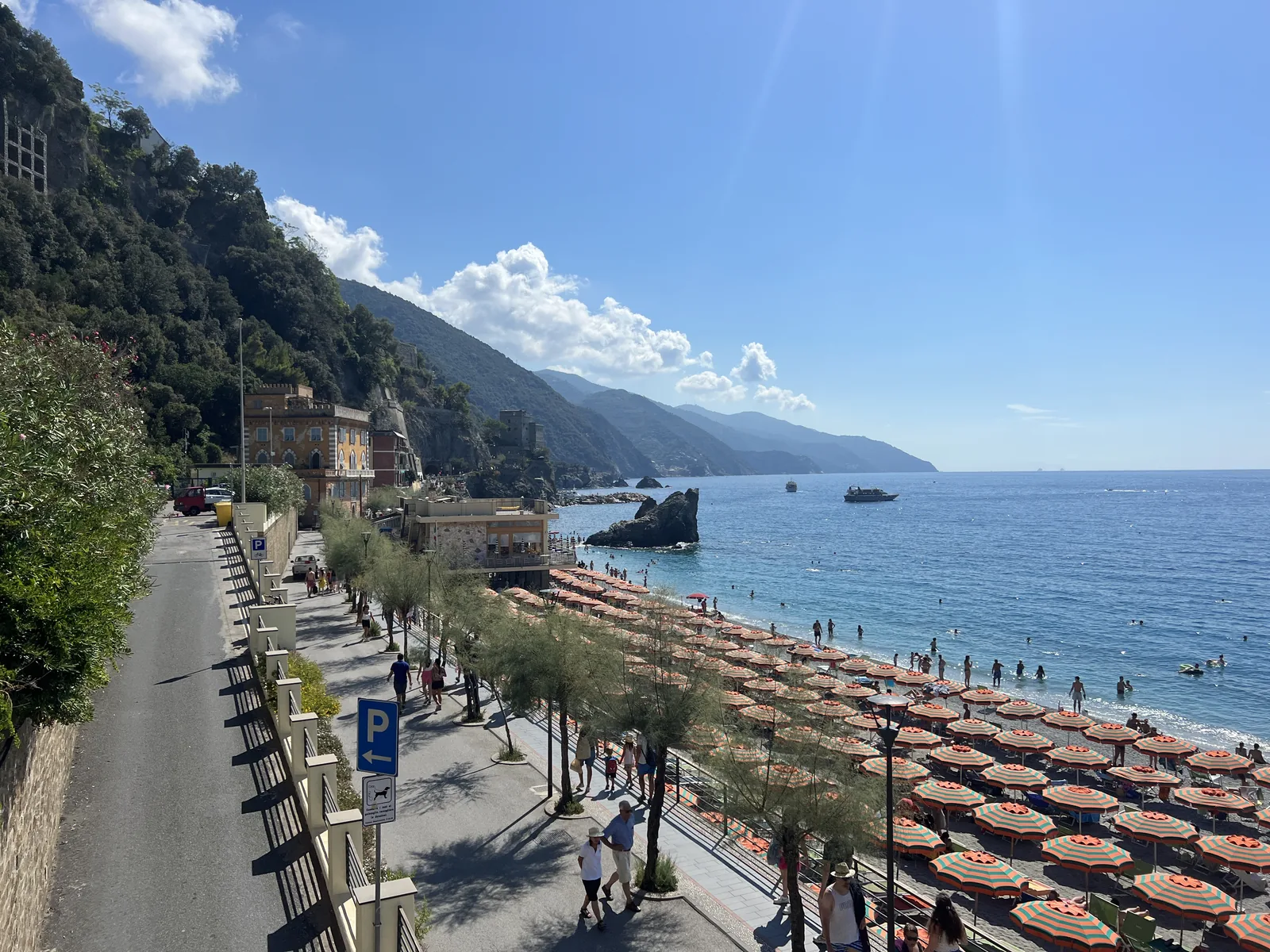 Uferpromenade in Monterosso al Mare über dem Strand von Fegina mit Reihen von Sonnenschirmen, dahinter die Küste Richtung Punta Mesco