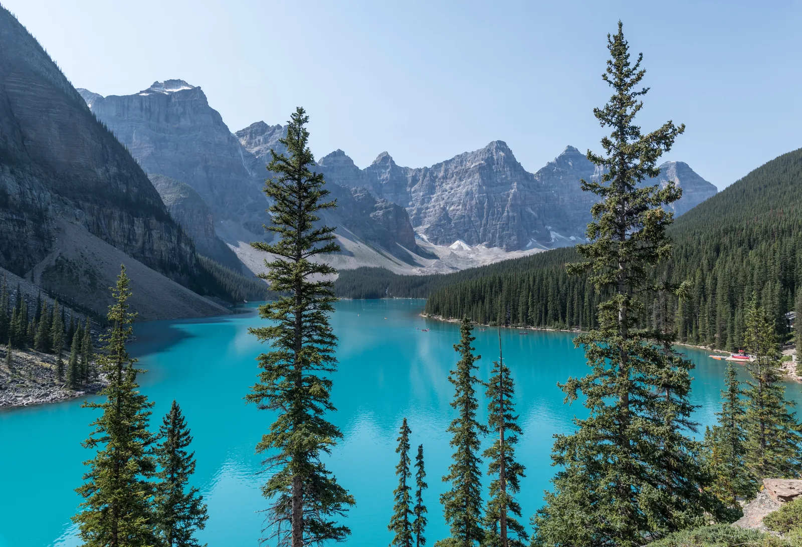 Türkisfarbener Moraine Lake zwischen Nadelbäumen, dahinter die Zehn Gipfel