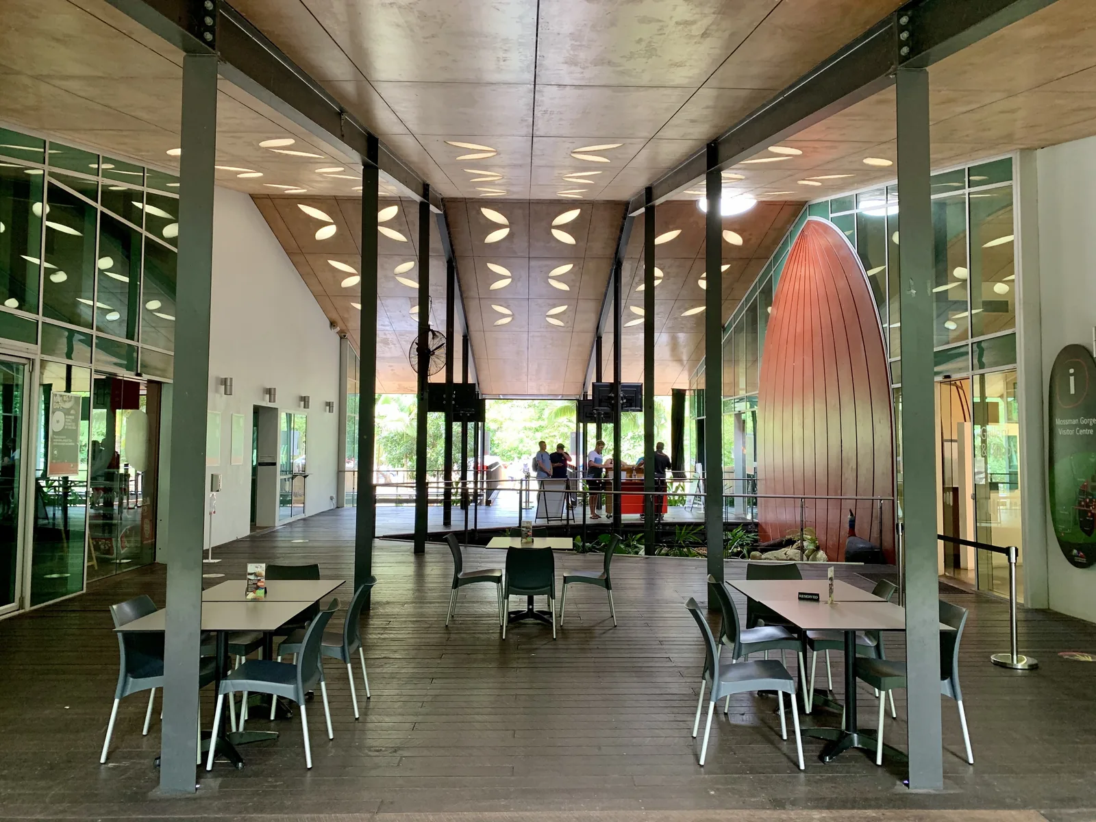 Die offene Halle des Mossman Gorge Centre mit Tischen, Glaswänden und einer hohen, kupferfarbenen Skulptur