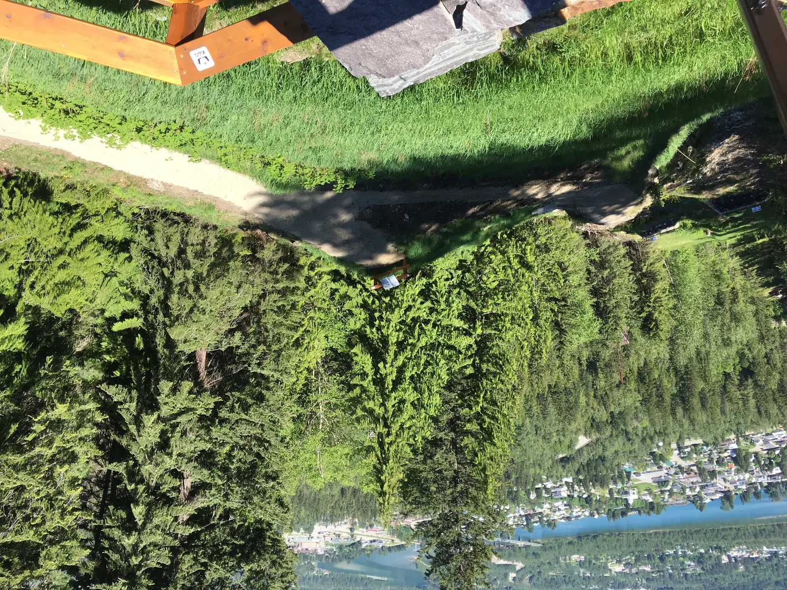 Blick vom Kopf der alten Sprungschanze den bewachsenen Hang hinab auf die Stadt Revelstoke und den Fluss, im Vordergrund ein Holzgeländer