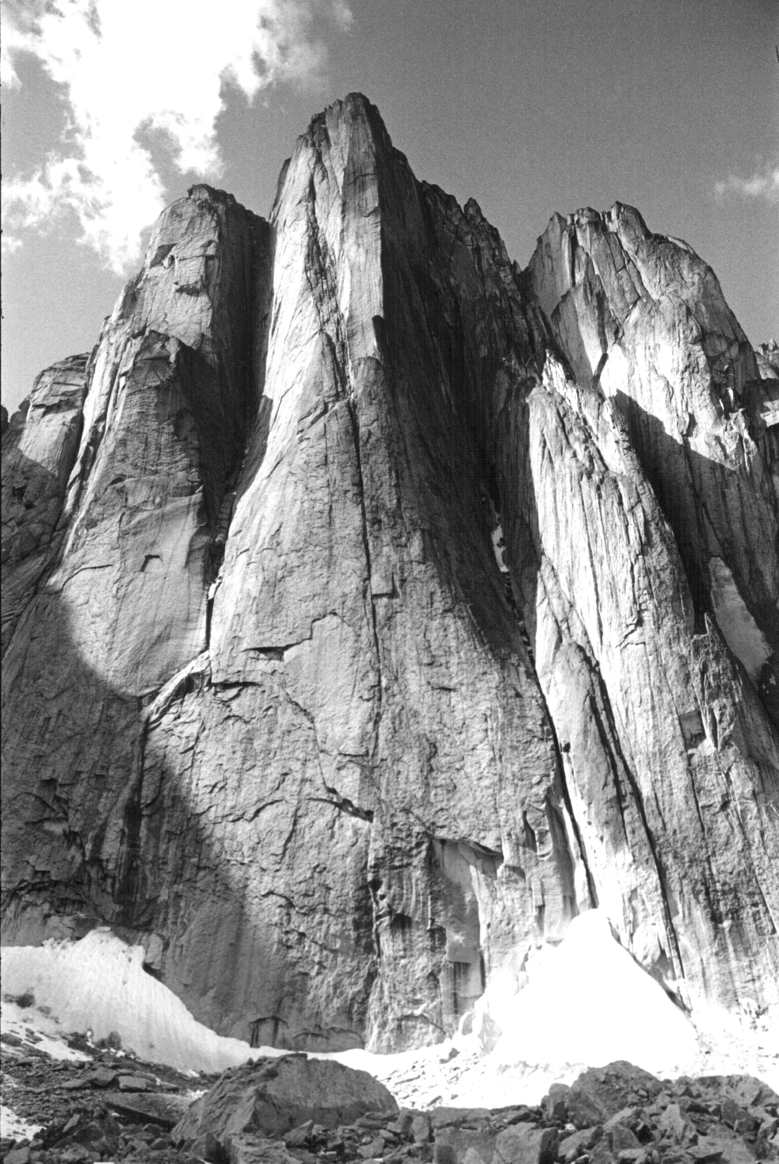 Schwarzweißaufnahme des Lotus Flower Tower: eine gewaltige senkrechte Granitwand steigt aus einem Schneefeld auf, daneben weitere Felstürme