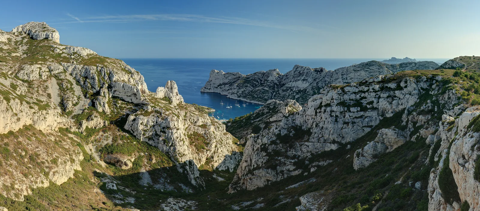Die Calanque de Sormiou im Nationalpark Calanques am späten Nachmittag: helle Kalkfelsen und grüne Hänge über dem Meer, hinten die Inseln