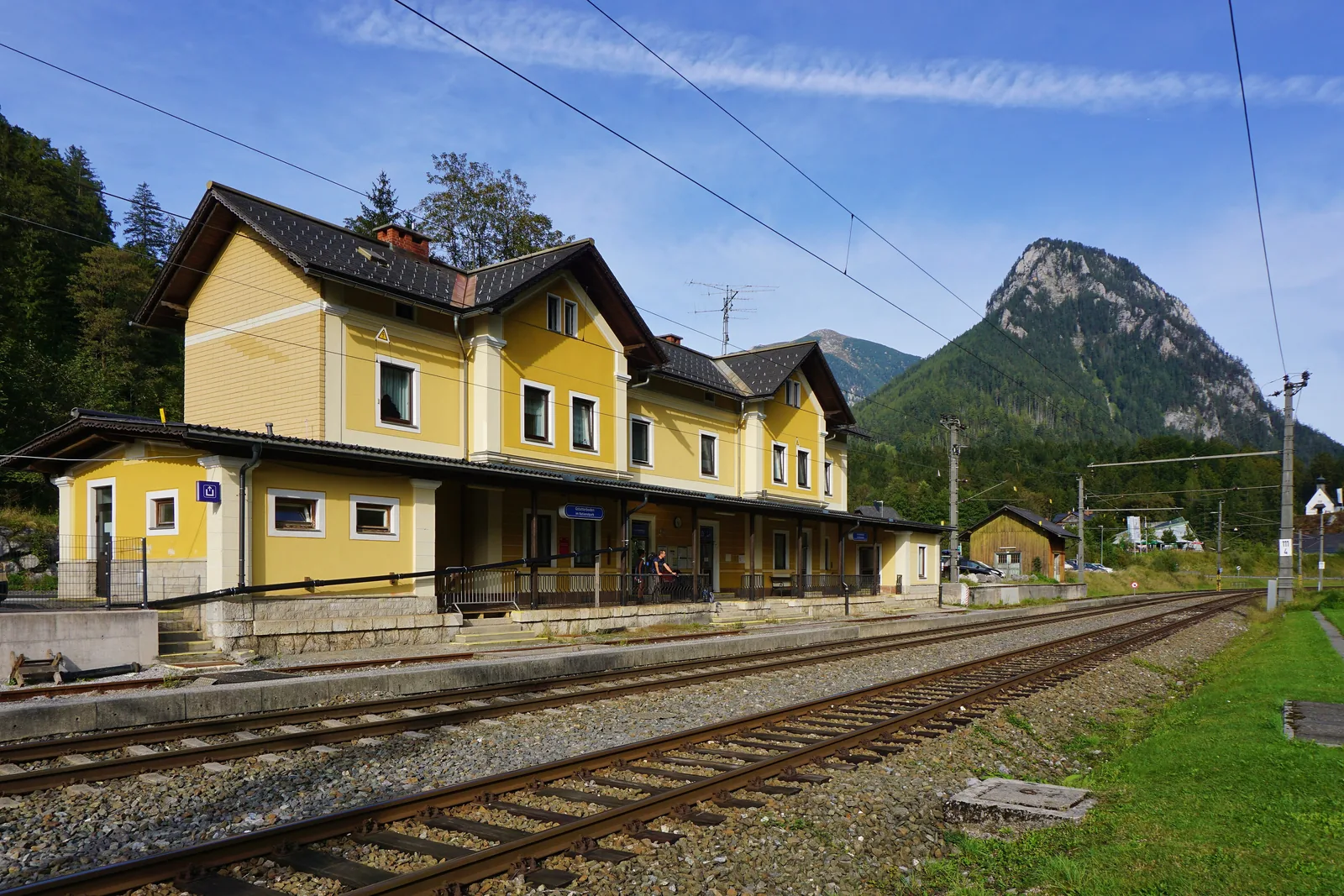 Der gelbe Bahnhof Gstatterboden im Nationalpark Gesäuse an der Gleisanlage, dahinter der bewaldete Gstatterstein