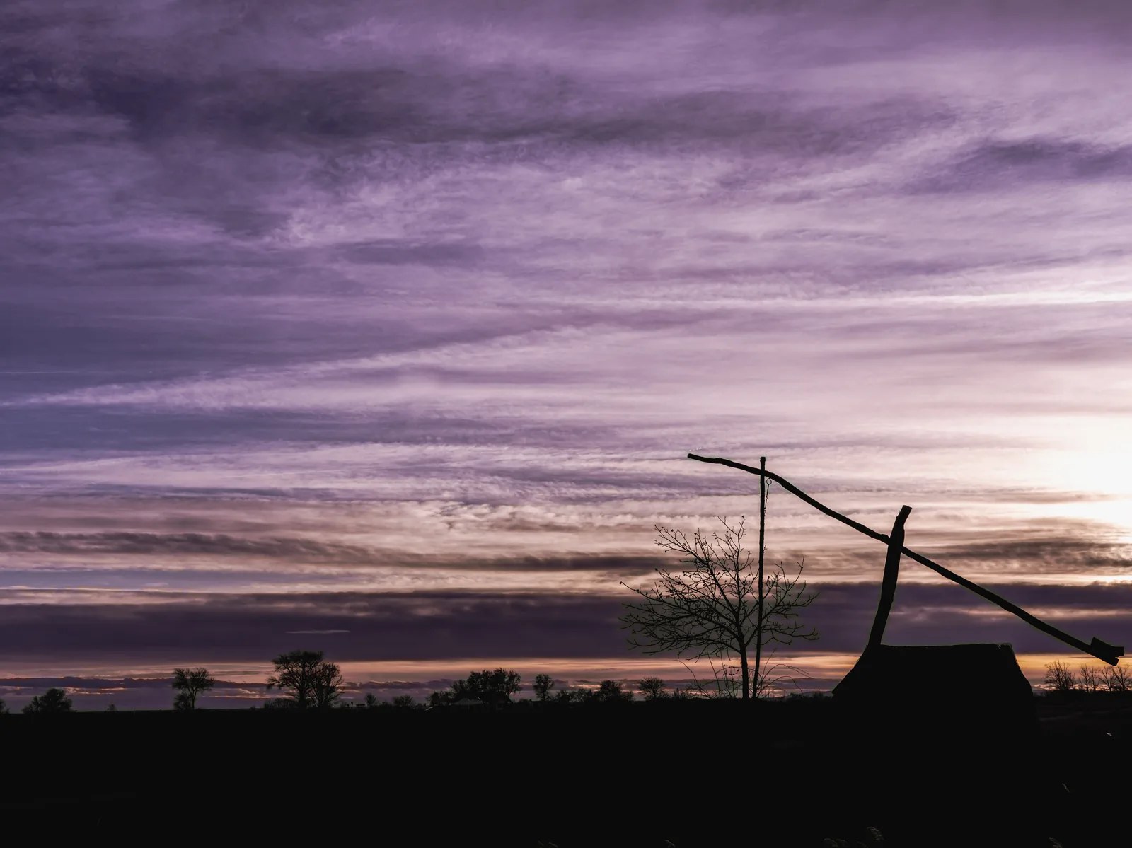 Ein Ziehbrunnen als Silhouette vor violettem Abendhimmel an der Langen Lacke im Nationalpark Neusiedler See – Seewinkel