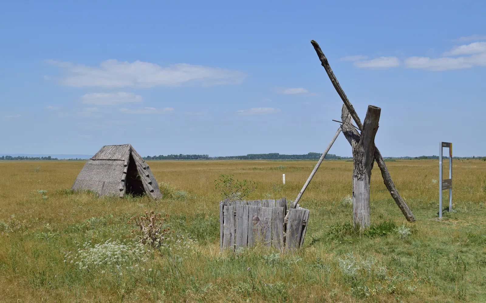 Ein hölzerner Ziehbrunnen und eine Schilfhütte auf der Hutweide an der Langen Lacke im Nationalpark Neusiedler See – Seewinkel