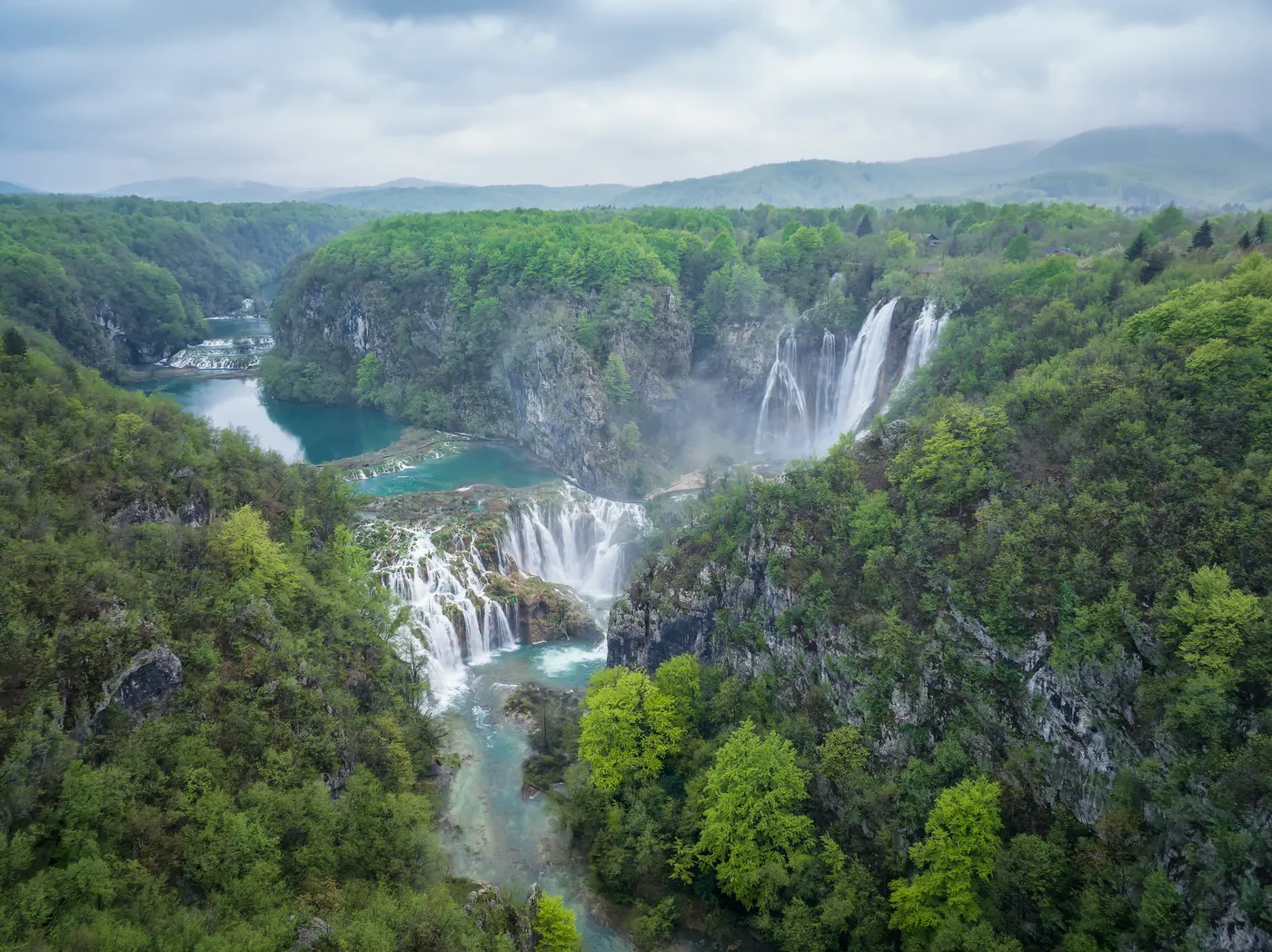 Luftaufnahme der Plitvicer Seen im Frühling: türkisfarbene Seen und Wasserfälle zwischen hellgrünem Laubwald
