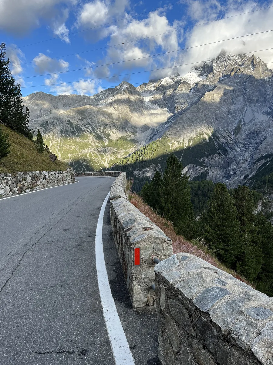 Eine Kehre der Stilfser-Joch-Straße im Nationalpark Stilfserjoch mit Steinmauer, dahinter Wald und vergletscherte Gipfel