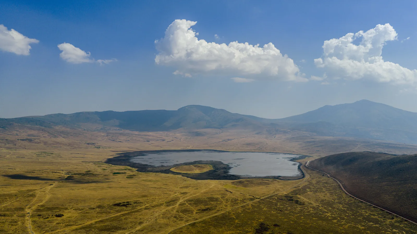 Der Ngorongoro-Krater aus der Luft: der helle Magadi-See auf dem Boden, ringsum die Kraterwände unter Wolken