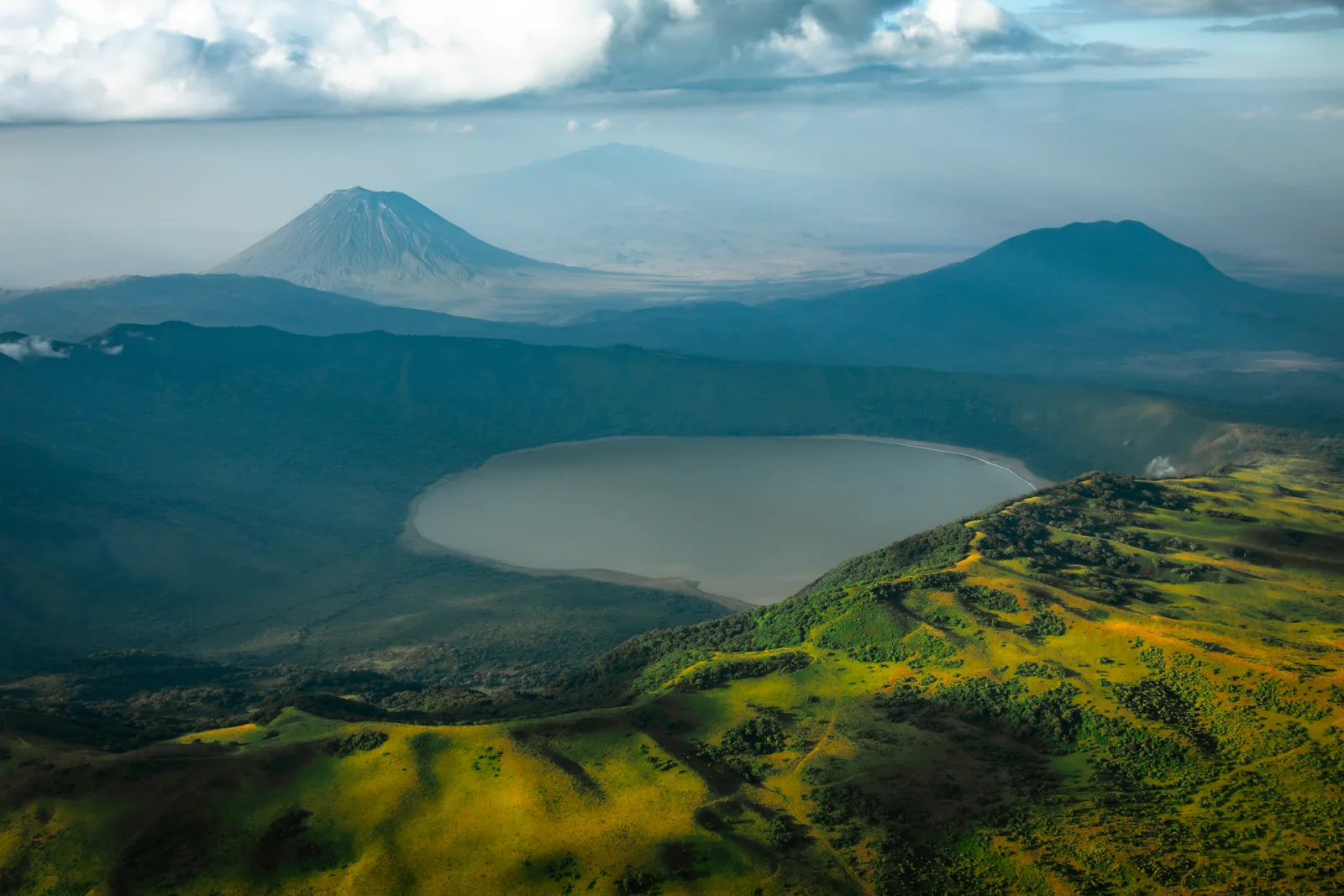 Der Kratersee des Empakaai zwischen grünen Wänden, am Horizont der Kegel des Ol Doinyo Lengai