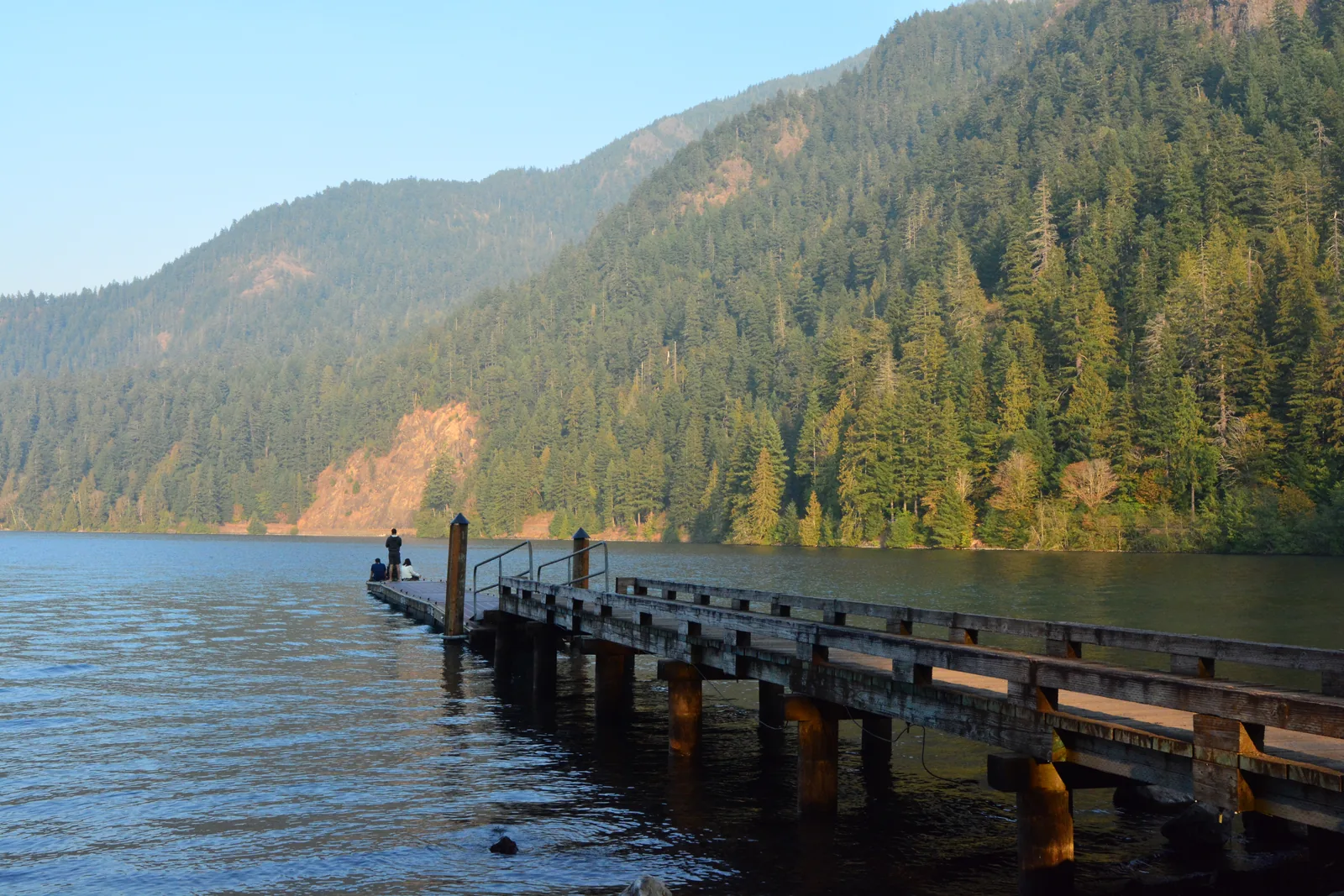 Holzsteg ins stille Wasser des Lake Crescent, dahinter bewaldete Berghänge im Abendlicht