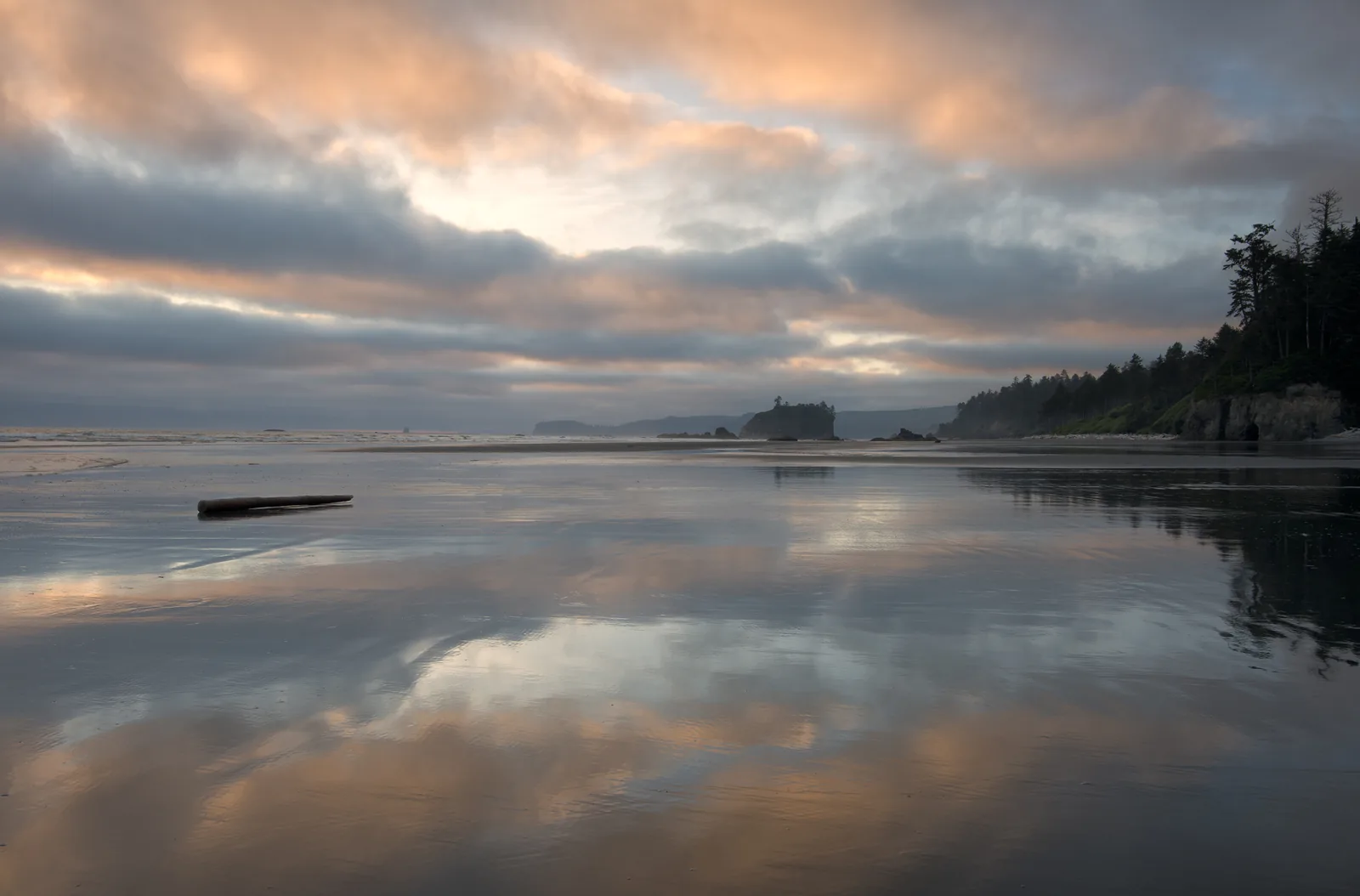 Ruby Beach bei Ebbe: nasser Sand spiegelt den Abendhimmel, dahinter Felstürme und die bewaldete Steilküste