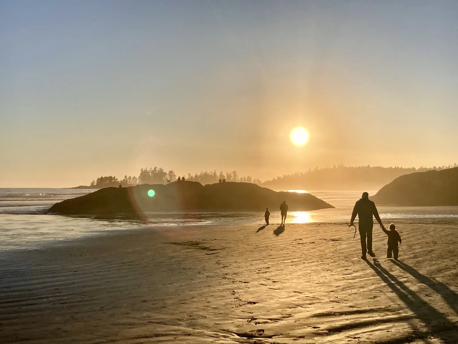 Familie als Silhouette auf dem weiten Sandstrand von Long Beach, tiefstehende Sonne über dem Pazifik