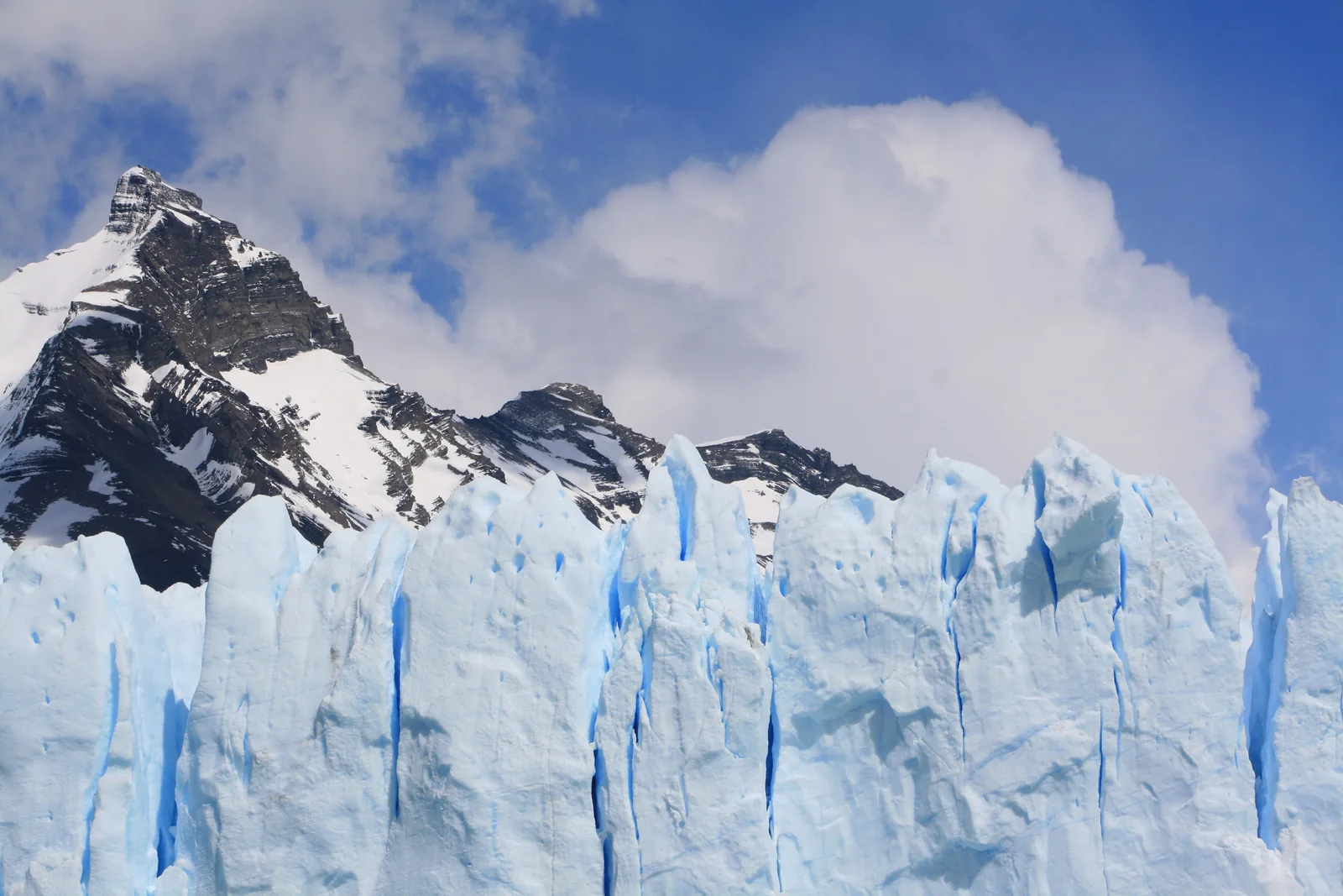 Hohe, blauweiße Eistürme an der Front des Perito-Moreno-Gletschers im Nationalpark Los Glaciares unter einem schroffen, verschneiten Gipfel