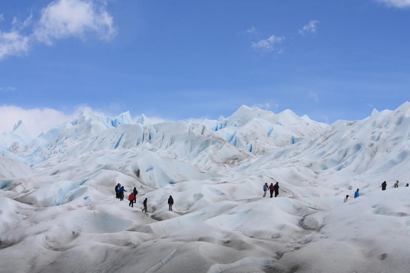 Wanderer mit Steigeisen auf dem Eis des Perito-Moreno-Gletschers im Nationalpark Los Glaciares zwischen weißen Eishügeln