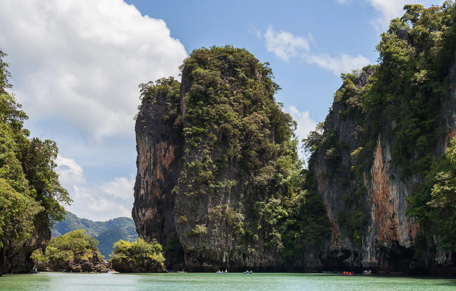 Steile, bewachsene Kalkfelsen von Ko Panak im Nationalpark Ao Phang Nga, davor flaches grünes Wasser und eine kleine Felsinsel