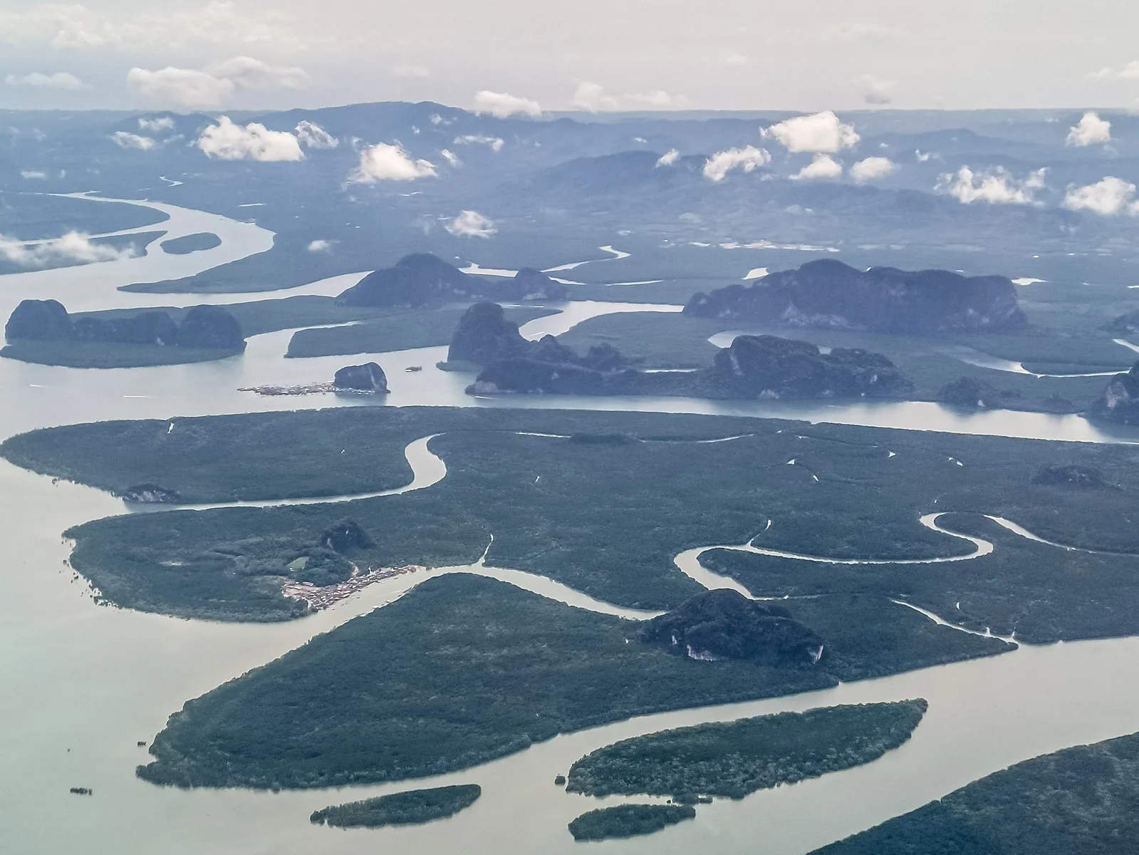 Luftbild der Phang-Nga-Bucht mit Mangroveninseln, gewundenen Wasserläufen und Kalkinseln unter Wolken