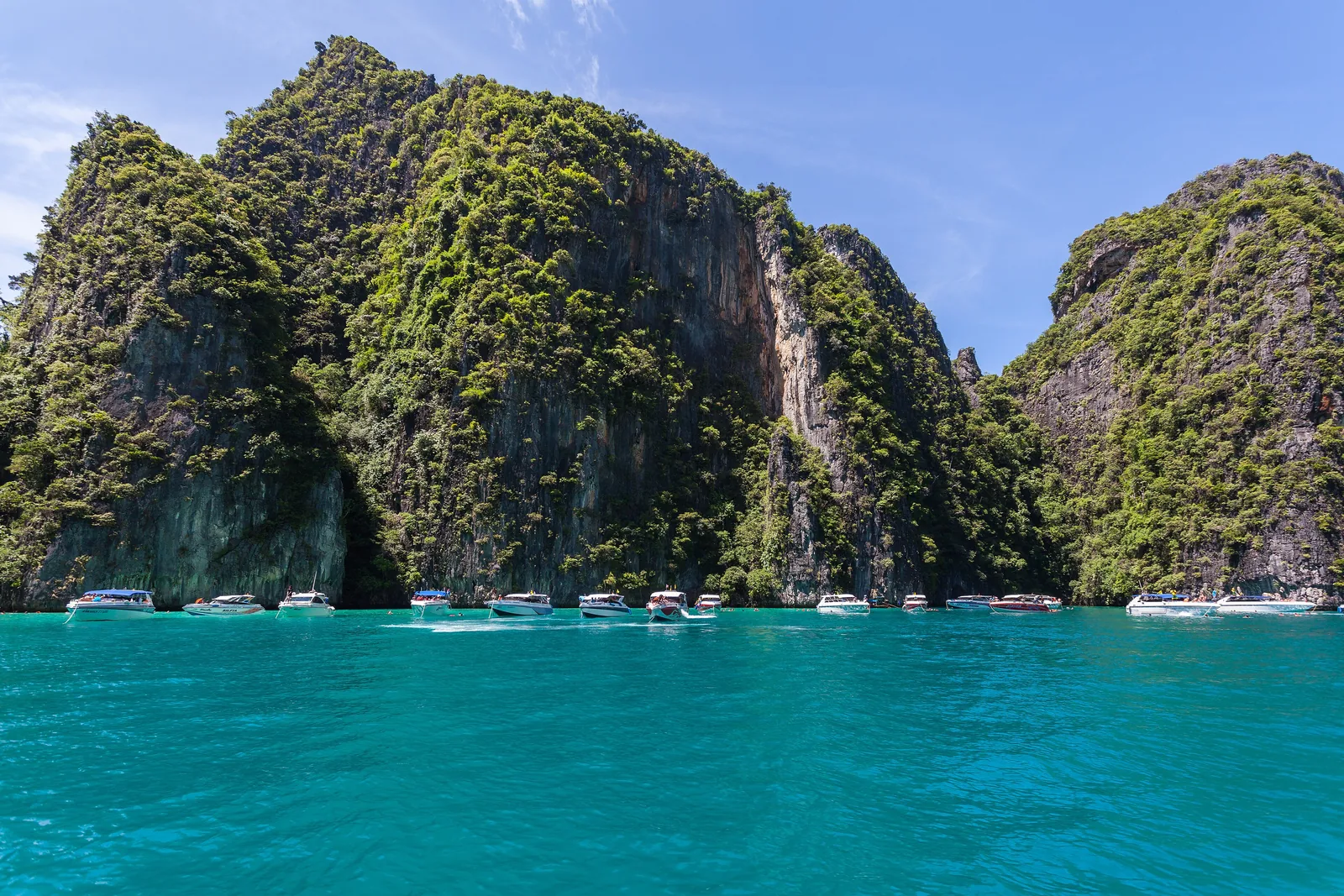 Senkrechte, dicht bewachsene Kalksteinwände von Ko Phi Phi Le im Phi-Phi-Nationalpark, davor eine Reihe Schnellboote auf türkisfarbenem Wasser