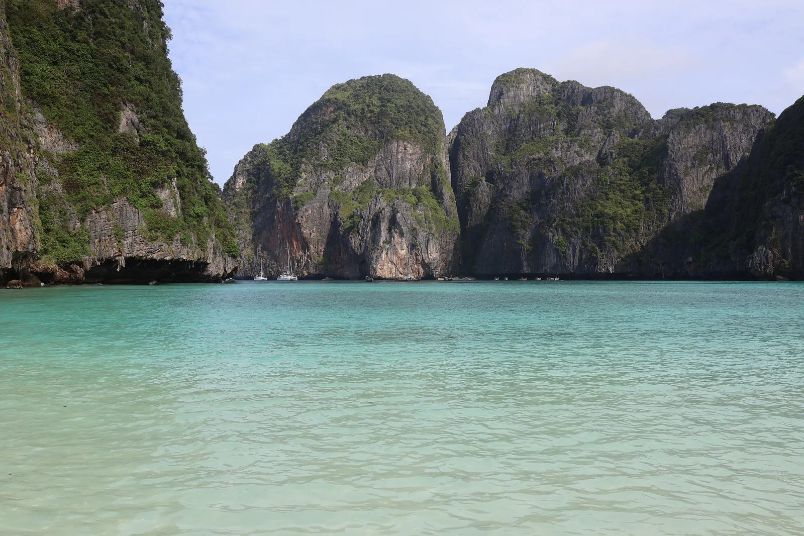 Flaches, hellgrünes Wasser in der Maya Bay im Phi-Phi-Nationalpark, dahinter die dunklen Kalkfelsen, die die Bucht umschließen