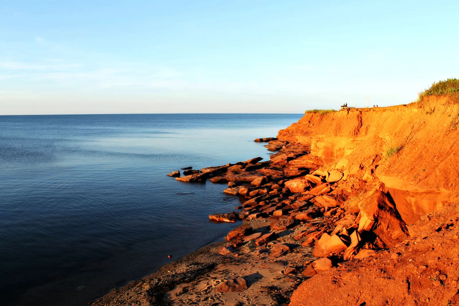 Rote Sandsteinklippen im tiefen Abendlicht fallen zu einem ruhigen, dunkelblauen Meer ab, am Fuß der Klippe liegen abgebrochene Felsplatten
