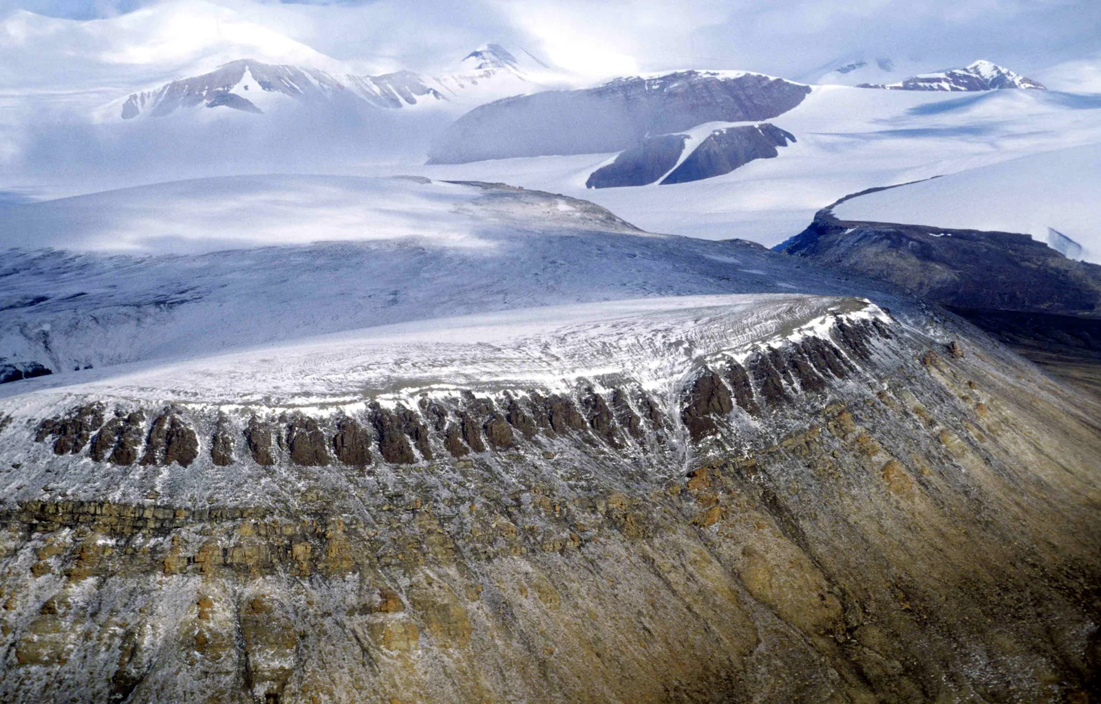 Aus einem weiten Eisfeld ragen dunkle, abgeschliffene Bergrücken heraus, im Vordergrund eine vereiste Felskante