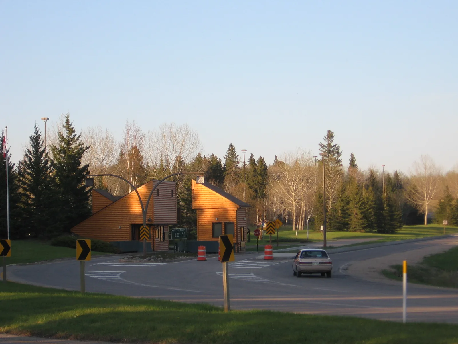 Das hölzerne Torgebäude des Parks am Highway 10 bei Wasagaming, davor die Fahrbahn mit einem passierenden Auto