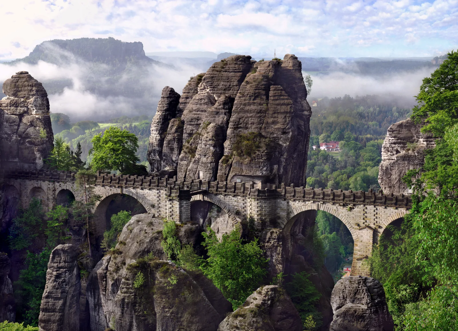 Die Basteibrücke spannt sich zwischen Sandsteintürmen, dahinter der Lilienstein über dem Elbtal