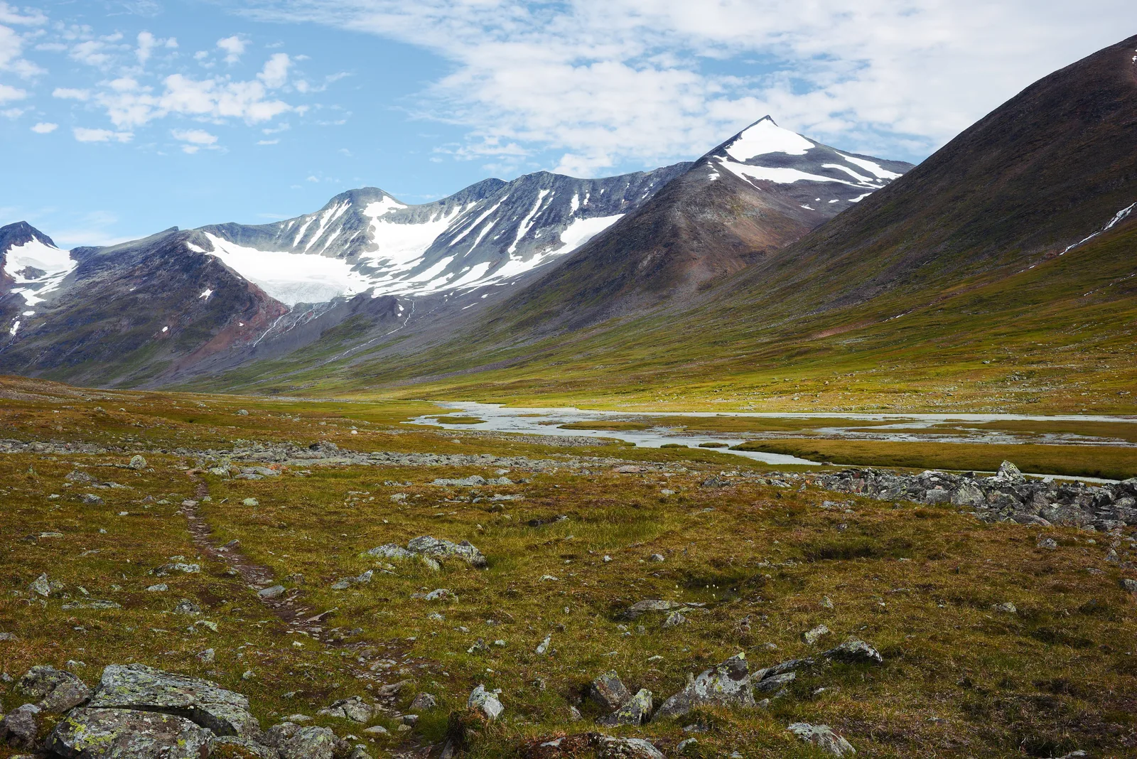 Ein Trampelpfad führt durch das weite Tal Ruohtesvágge im Sarek-Nationalpark auf schneebedeckte Gipfel und einen Gletscher zu