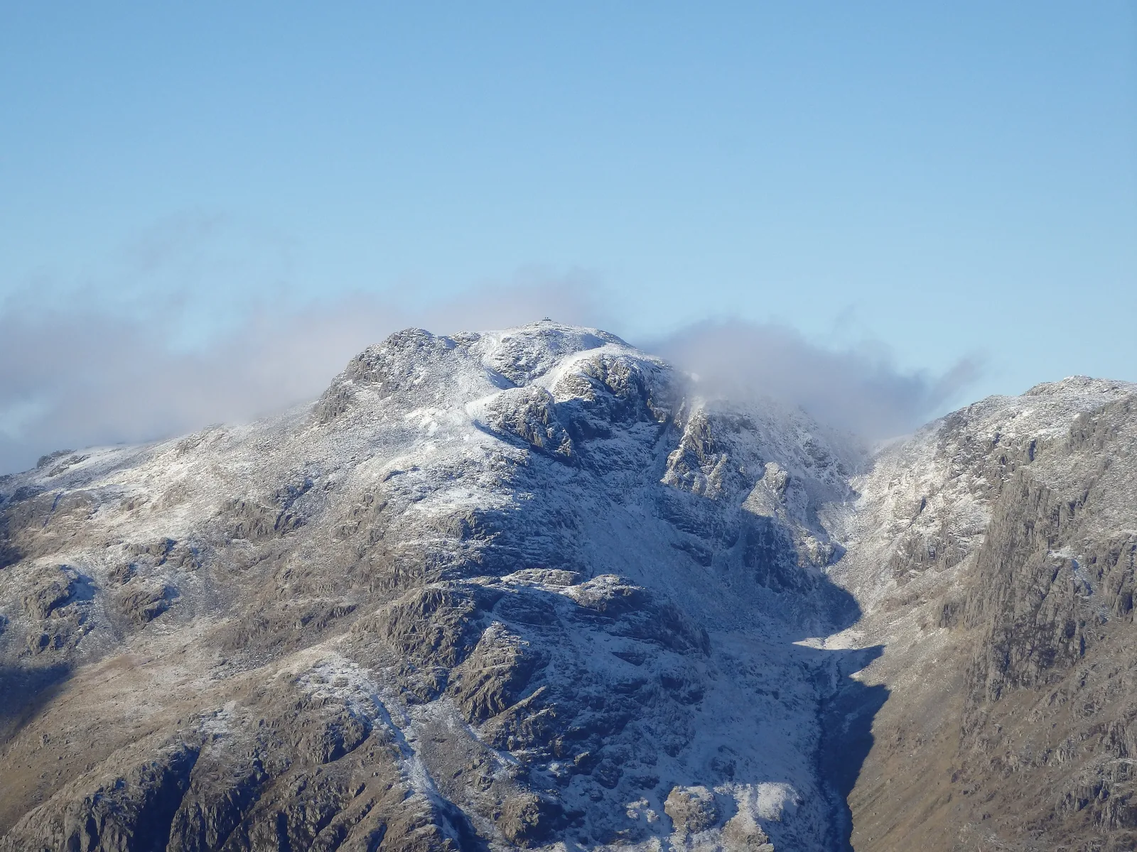 Der verschneite Scafell Pike im Lake-District-Nationalpark unter Wolken, gesehen von den Crinkle Crags