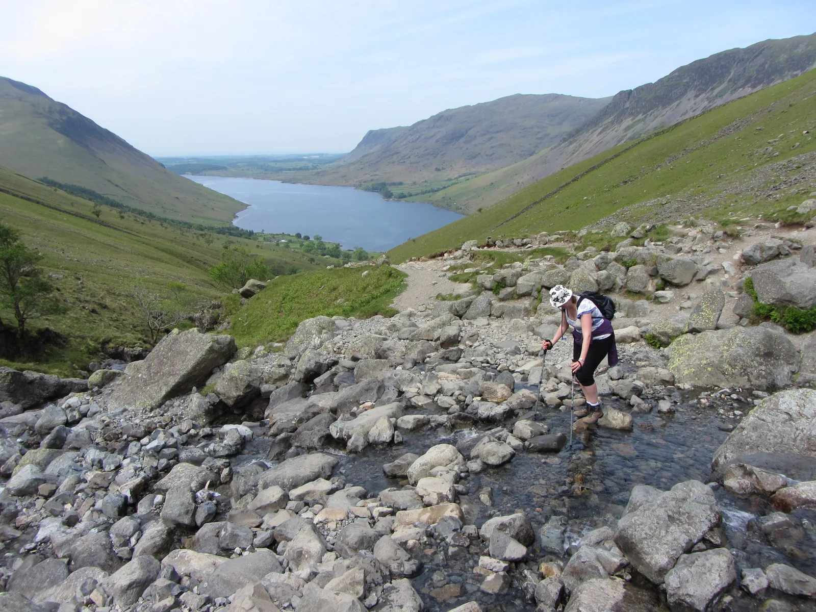 Ein Wanderer quert den Bach Lingmell Gill am Weg zum Scafell Pike, dahinter Wast Water im Lake-District-Nationalpark