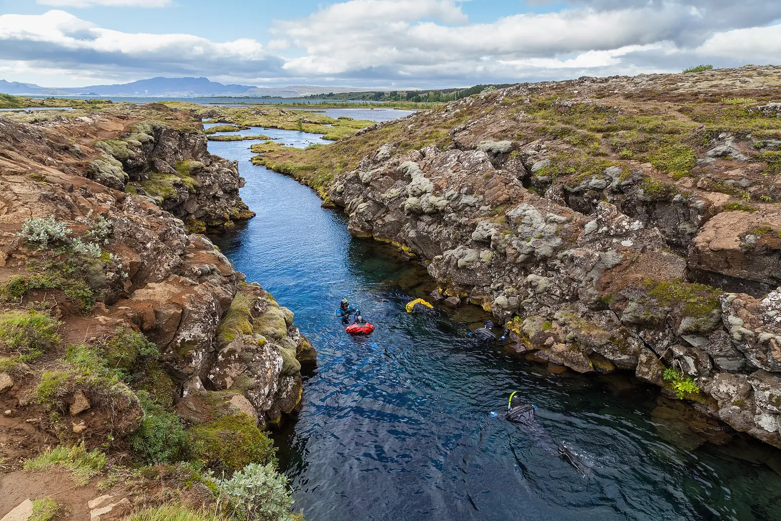 Schnorchler in der Silfra-Spalte im Nationalpark Þingvellir treiben durch klares blaues Wasser zwischen moosbewachsenen Lavafelsen
