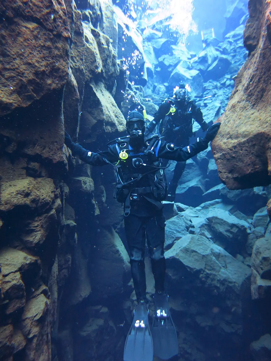 Ein Taucher im Trockenanzug schwebt in der Silfra zwischen zwei Felswänden im blauen Wasser