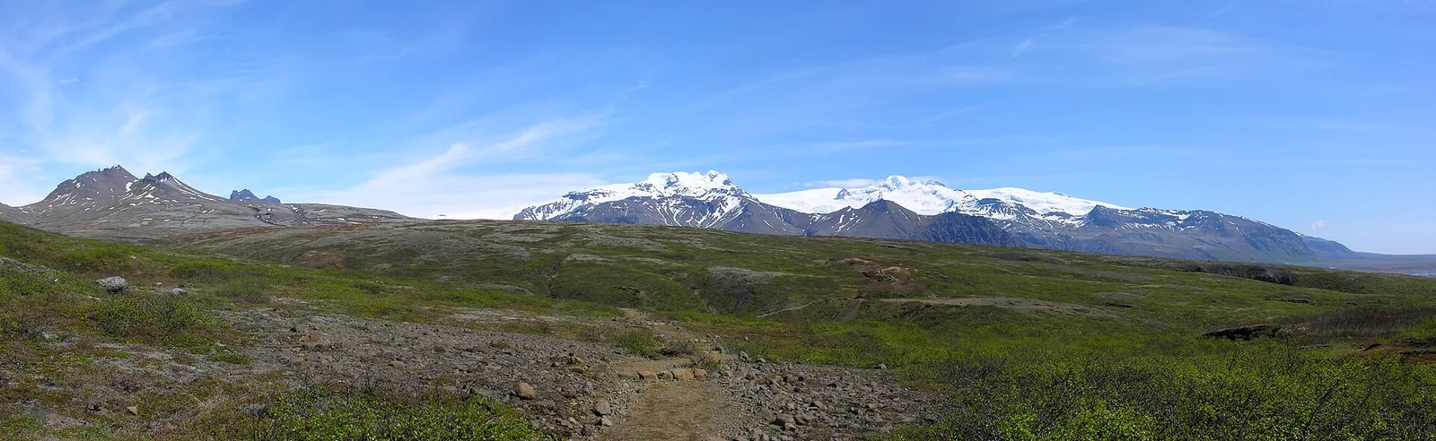 Der Weg zum Svartifoss in Skaftafell führt über grüne Hänge, im Hintergrund der Hafrafell und verschneite Gipfel