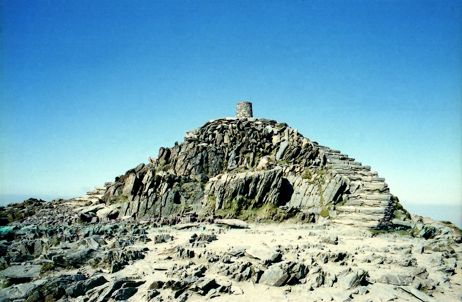 Der felsige Gipfel des Snowdon (Yr Wyddfa) im Snowdonia-Nationalpark mit dem Steinsockel und Stufen unter blauem Himmel