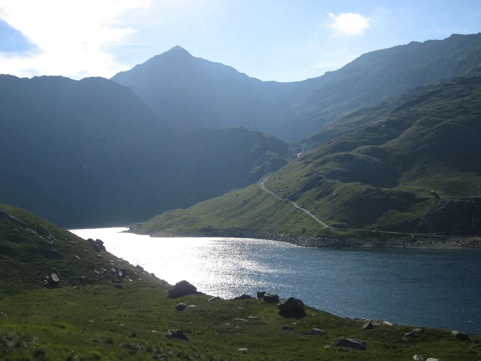 Der See Llyn Llydaw im Snowdonia-Nationalpark im Gegenlicht, darüber der spitze Gipfel des Snowdon (Yr Wyddfa)