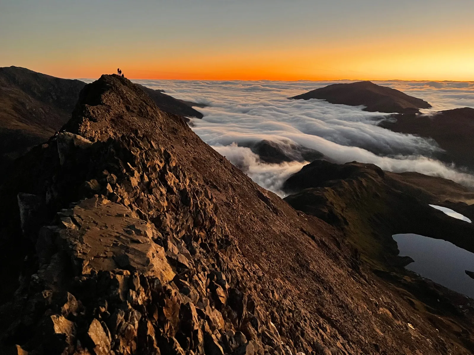 Sonnenaufgang über einem Wolkenmeer am Grat Crib Goch im Snowdonia-Nationalpark