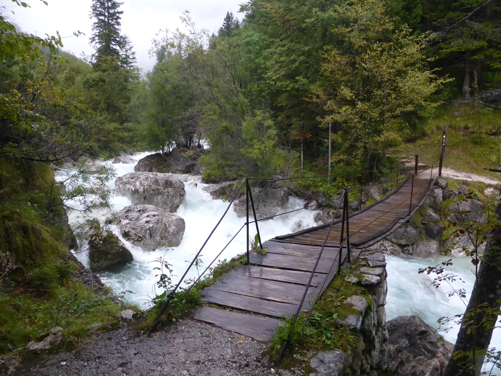 Ein Holzsteg führt am Soča-Weg über schäumendes Wasser