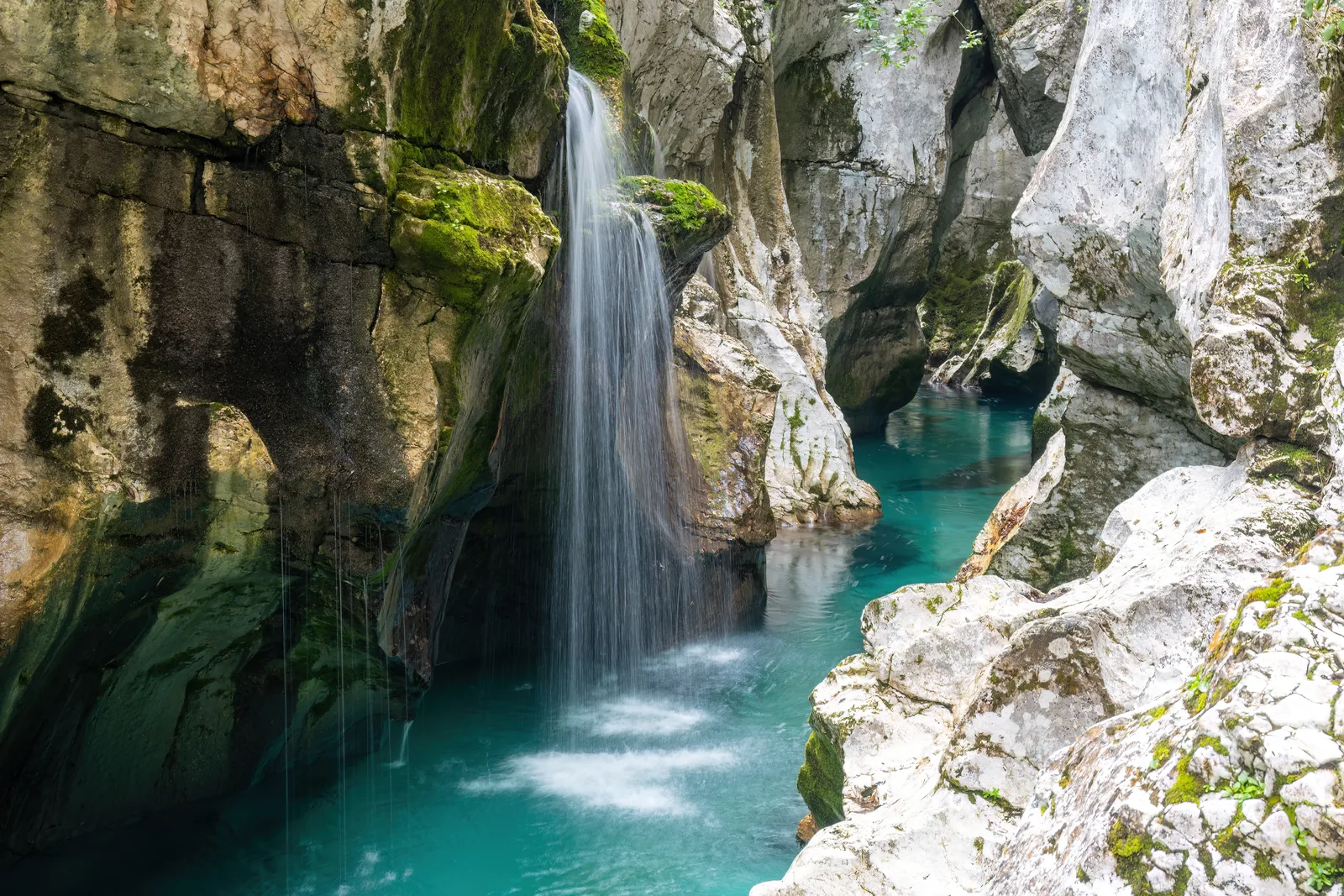 Ein Wasserfall stürzt in die türkisfarbene Soča zwischen hellen, ausgewaschenen Felswänden der Großen Tröge