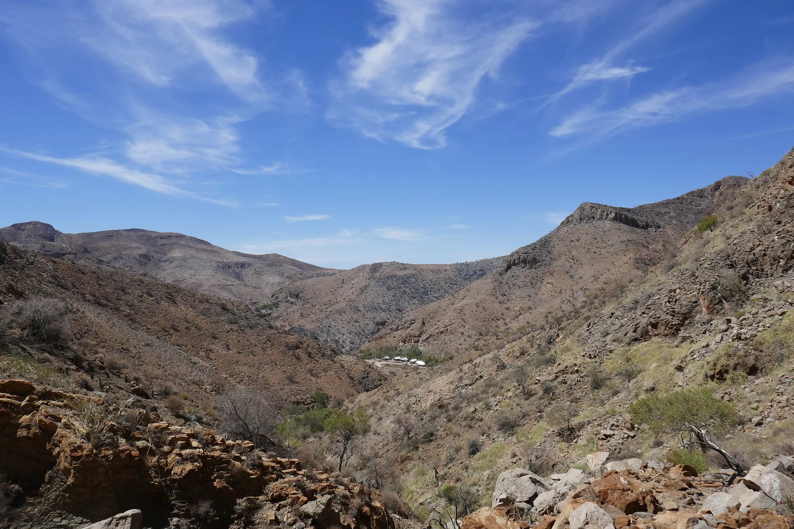 Felsige Bergkämme und ein Tal mit Akazien in den Naukluftbergen in Namibia unter blauem Himmel