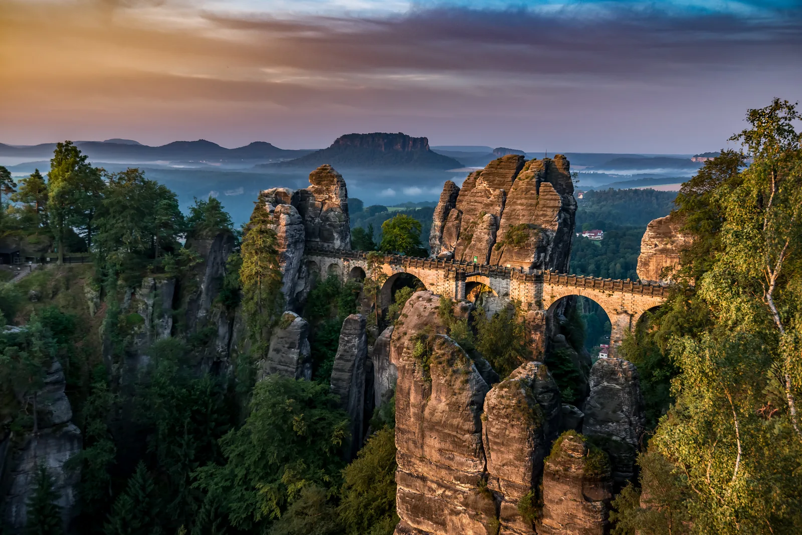 Die Basteibrücke im Abendlicht über den Sandsteintürmen, im Dunst der Lilienstein