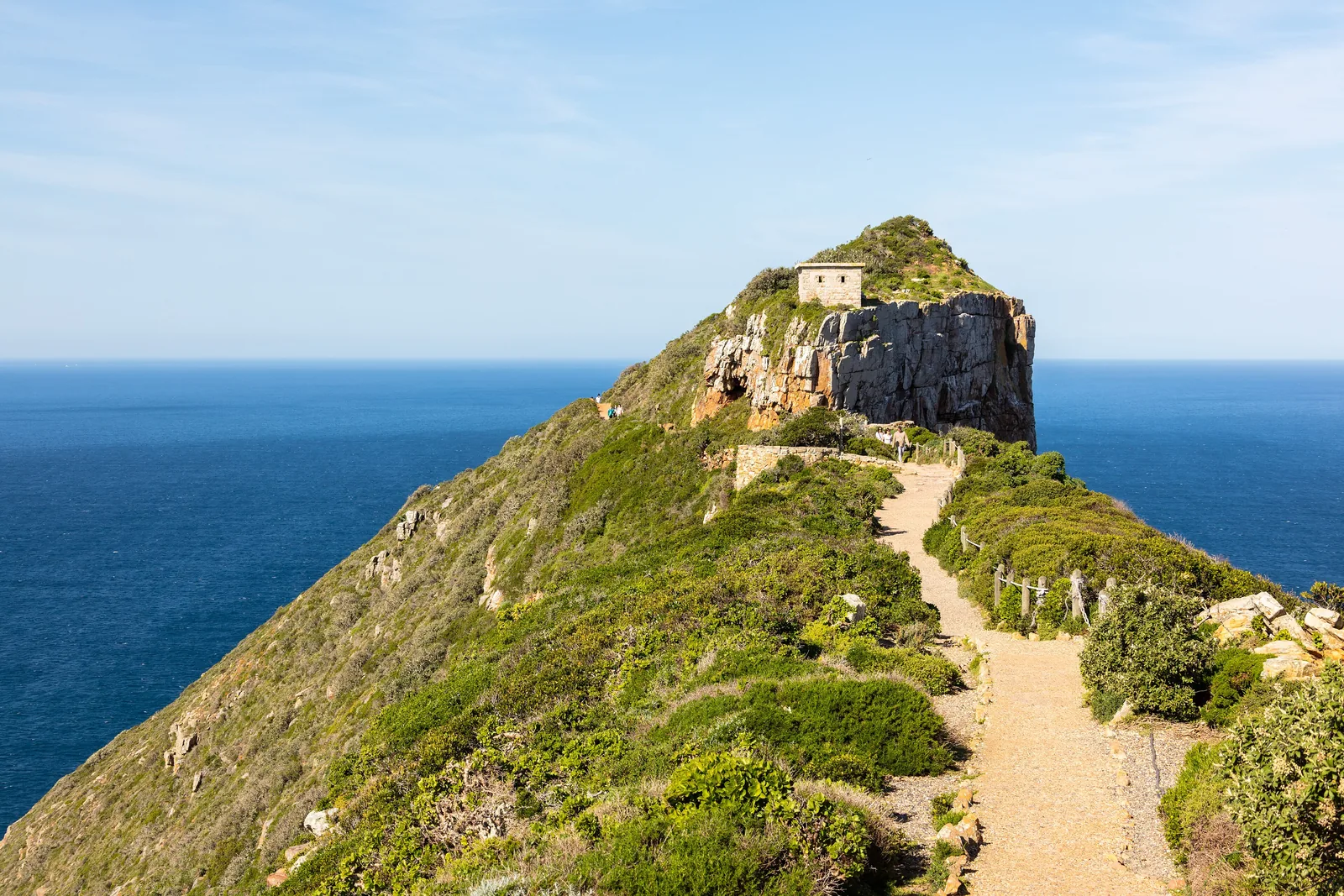 Ein Pfad führt im Tafelberg-Nationalpark über einen grünen Grat zum alten Leuchtturm auf dem Gipfel von Cape Point, dahinter das Meer