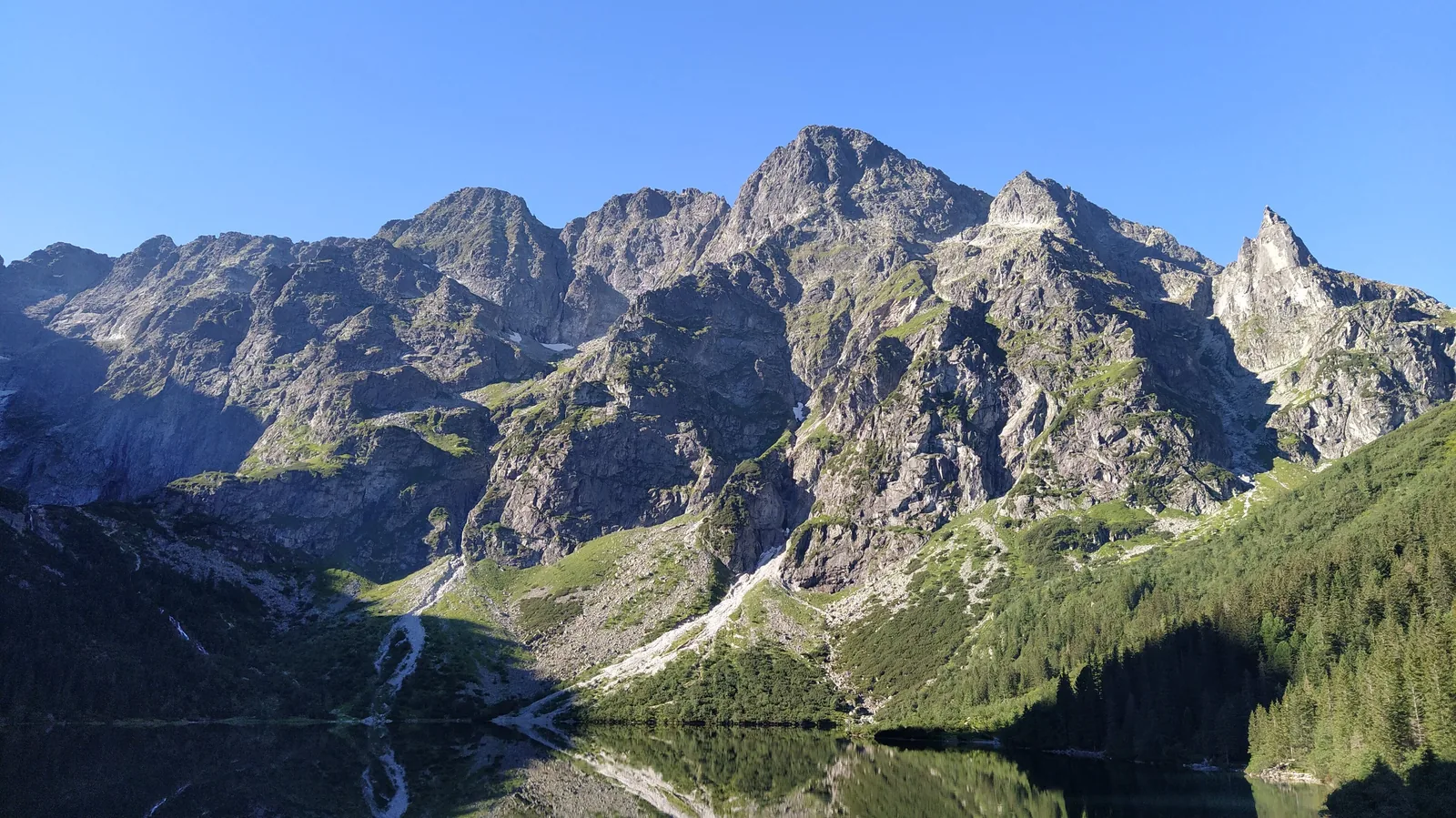 Blick über den Morskie Oko im Tatra-Nationalpark auf die Felswände der Hohen Tatra bei klarem Himmel, aufgenommen nahe der Schutzhütte